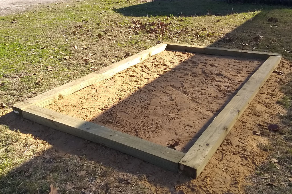 rectangular wooden frame base of the greenhouse filled with sand.