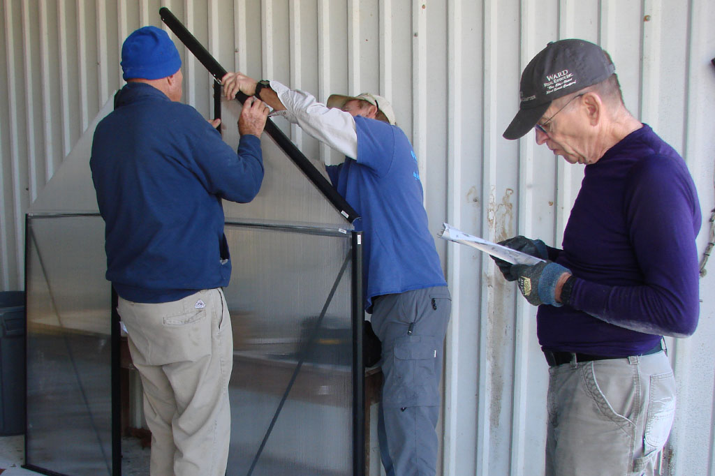 two men positioning a slanted panel while another person in the background reads instructions.