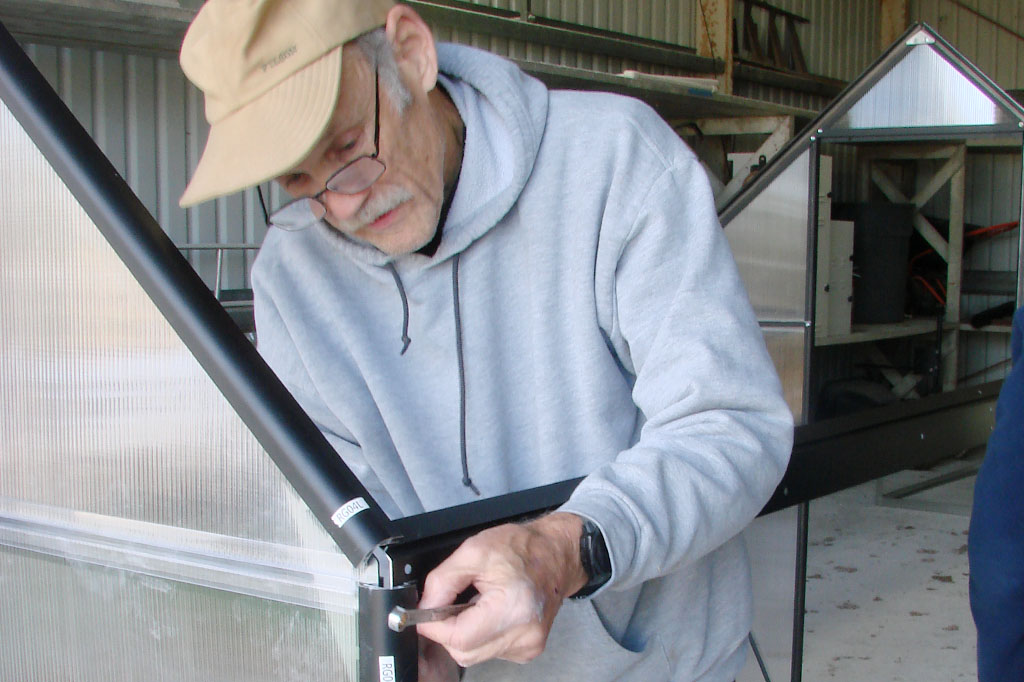 A man tightening a bolt on the greenhouse frame.