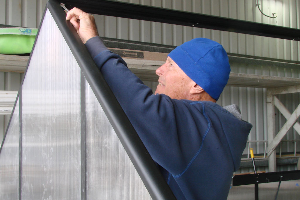 Another man tightening a bolt on the greenhouse frame.