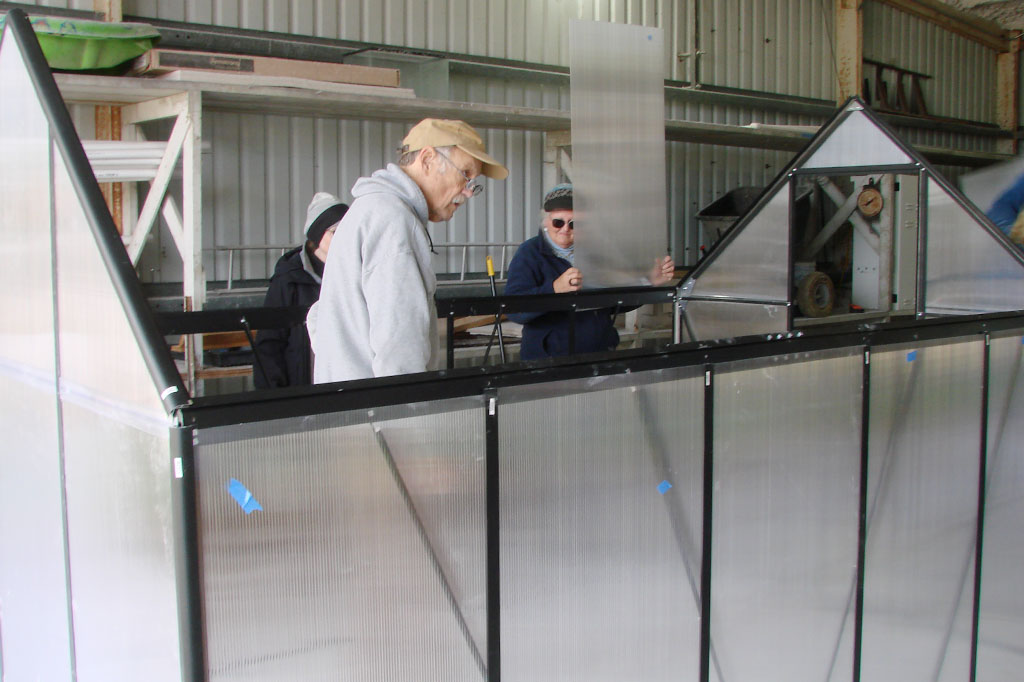 Three people working on assembling the greenhouse