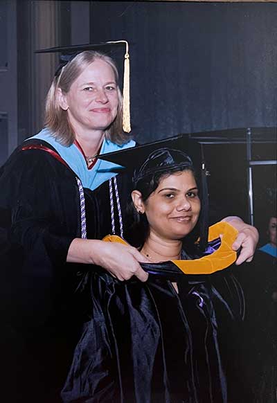 A woman places an academic regalia hood over another woman's head at a graduation ceremony.