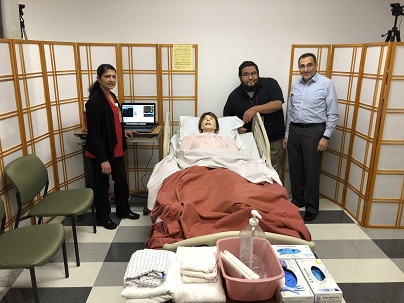 Three people standing next to a simulation manikin laying down on a hospital bed